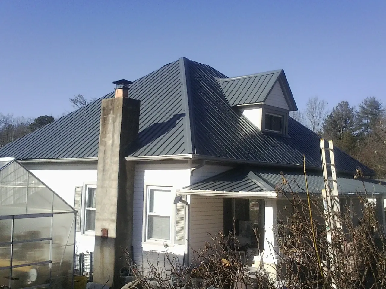 Dark blue standing seam metal roof on a white farmhouse with dormer — Slate & Tile Roof Repair by Roofing Brothers in Alta Vista