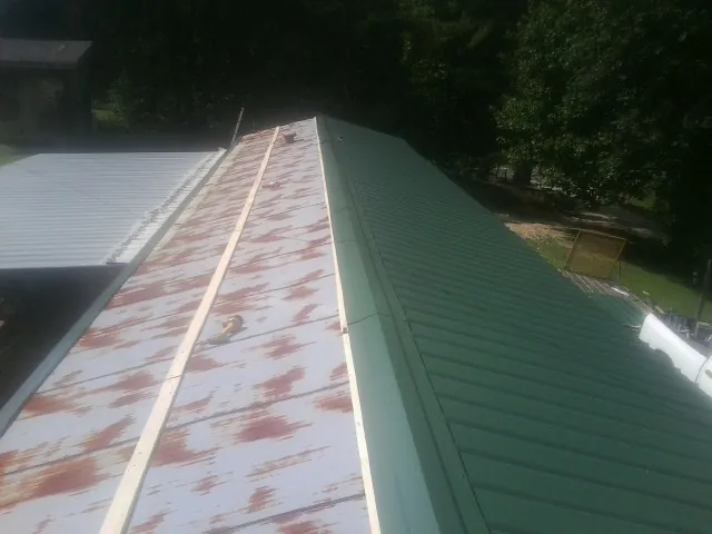 Old rusted panels beside newly installed green metal roofing — Wind Damage Roof Repair by Roofing Brothers in Alta Vista