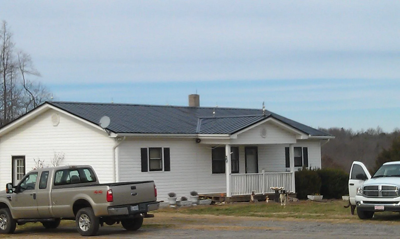 Finished dark metal roof on a white ranch home with work trucks parked in Alta Vista