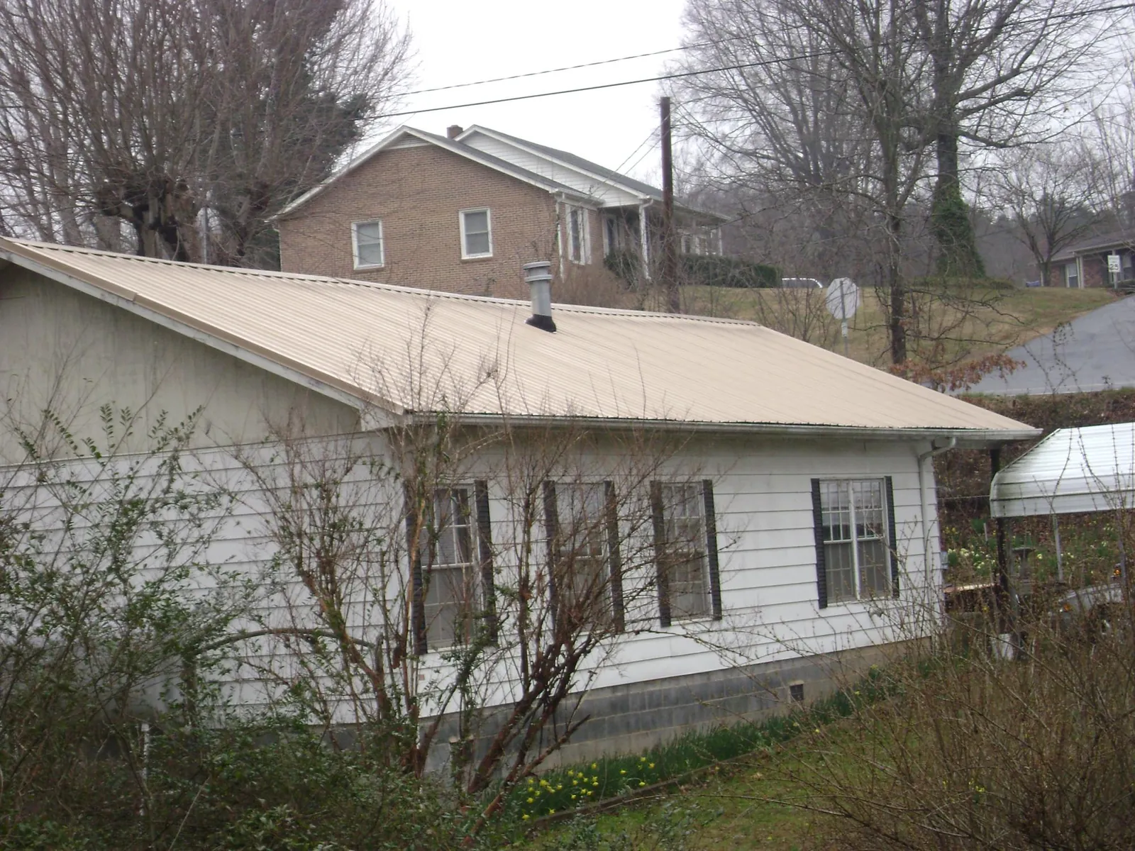 Tan metal roof on a white sided house set into a hillside — Commercial Roofing by Roofing Brothers in Alta Vista